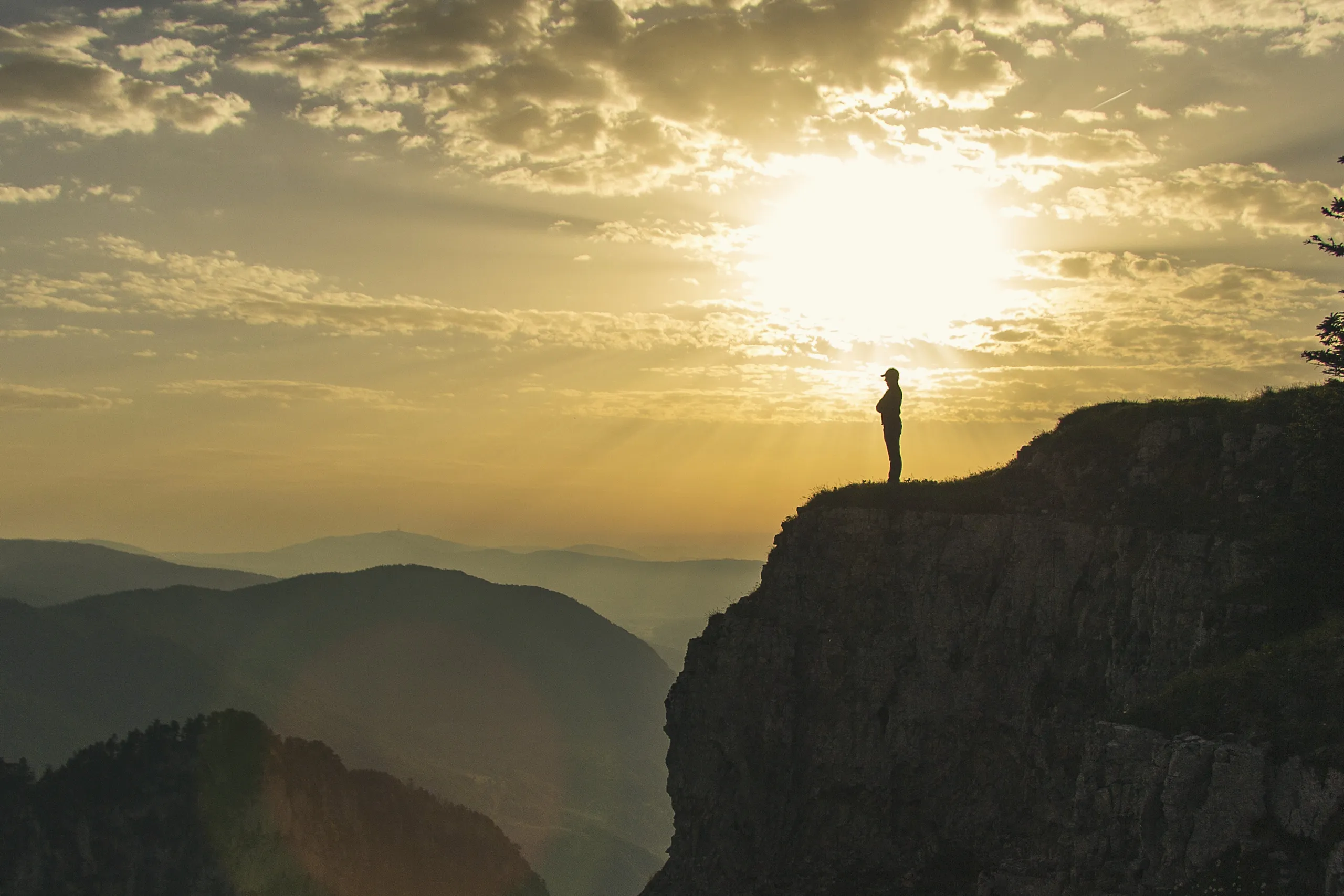 A hiker on the cliff edge of the Creux du Van at sunrise