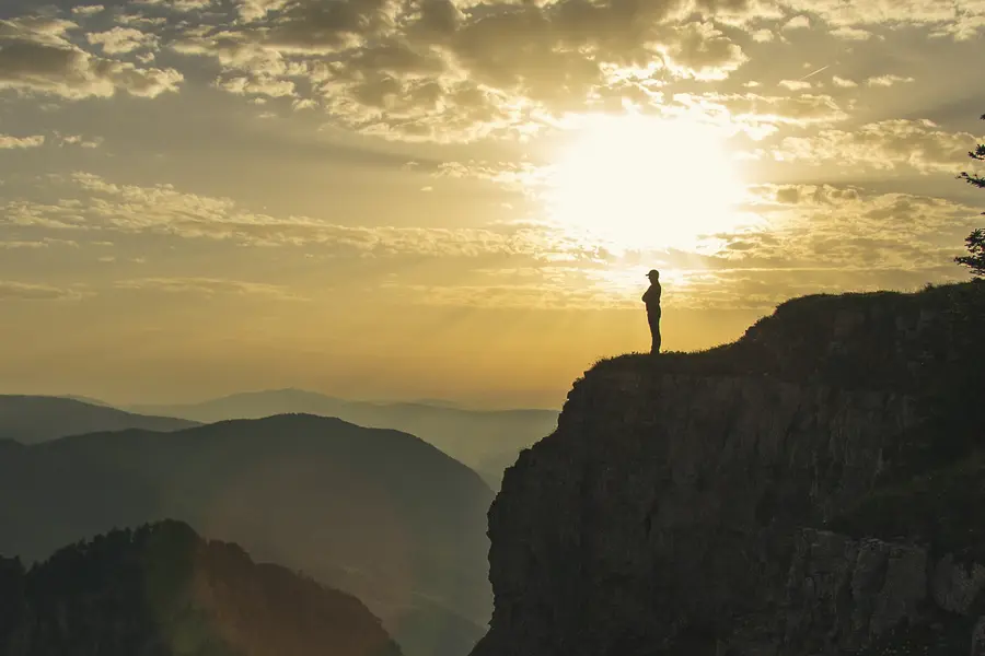 A hiker on the cliff edge of the Creux du Van at sunrise