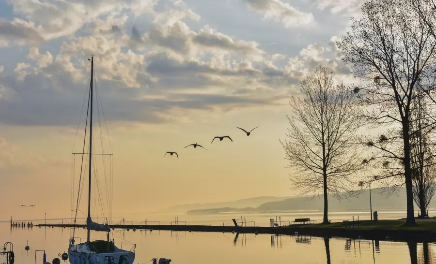 The lakeshore at sunrise, with the harbour and a moored sailboat